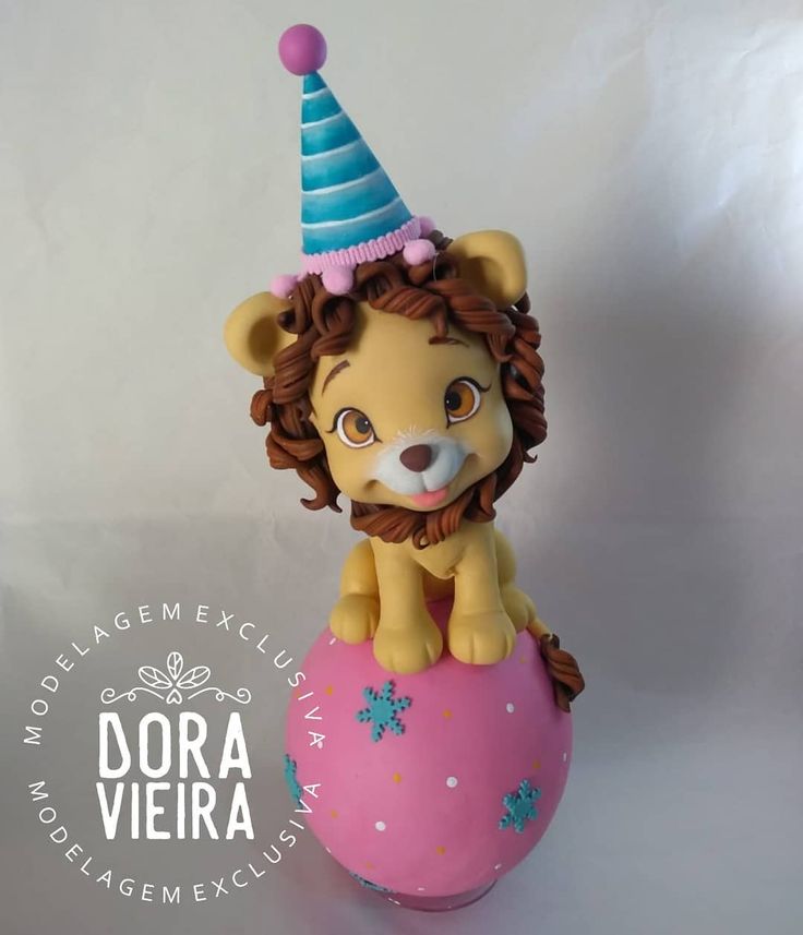 a lion figurine sitting on top of a pink ball with a blue hat