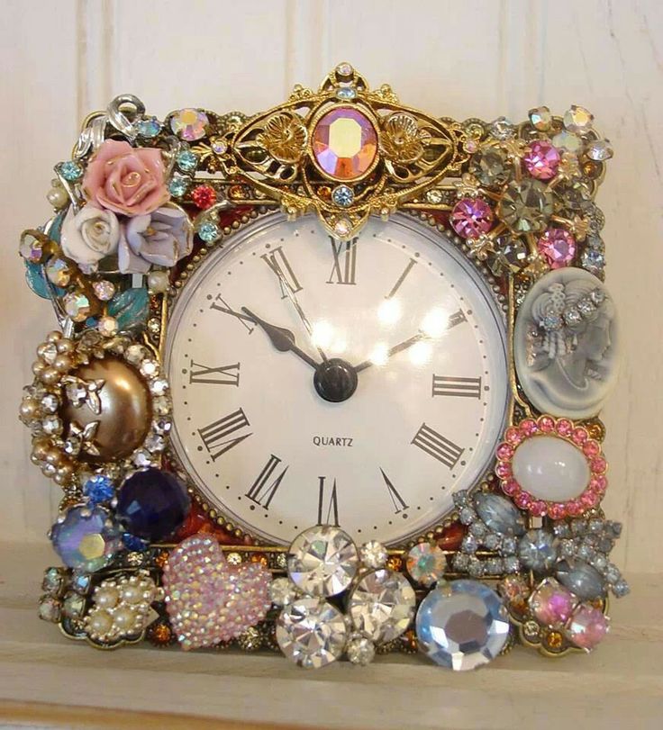 an ornate clock with jewels and flowers on it's face sits on a shelf