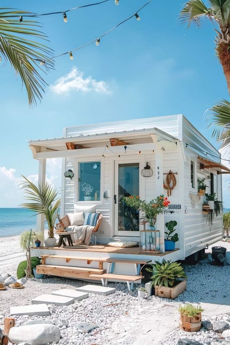 a small white house on the beach with plants and potted plants in front of it