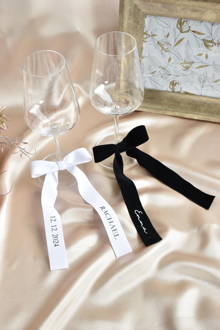 two empty wine glasses sitting next to each other on a satin covered table cloth with ribbon