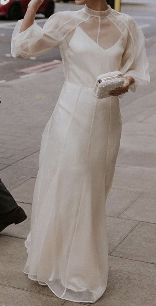 a woman in a white dress walking down the street talking on her cell phone while holding a purse