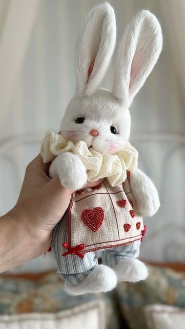 a hand holding a white stuffed rabbit with red hearts on it's chest and collar