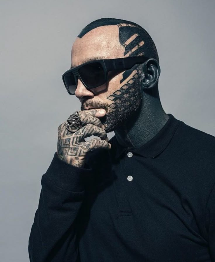 a man with tattoos on his face and arm, wearing black shirt and sunglasses looking to the side