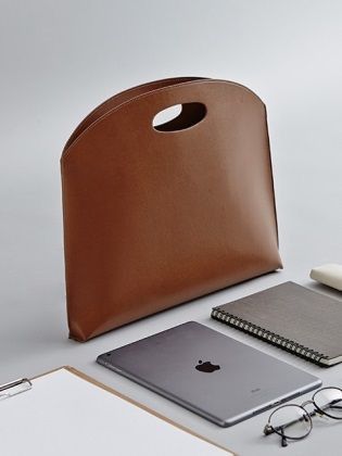 an apple laptop, notebook and pen sitting on top of a white table next to a brown leather bag