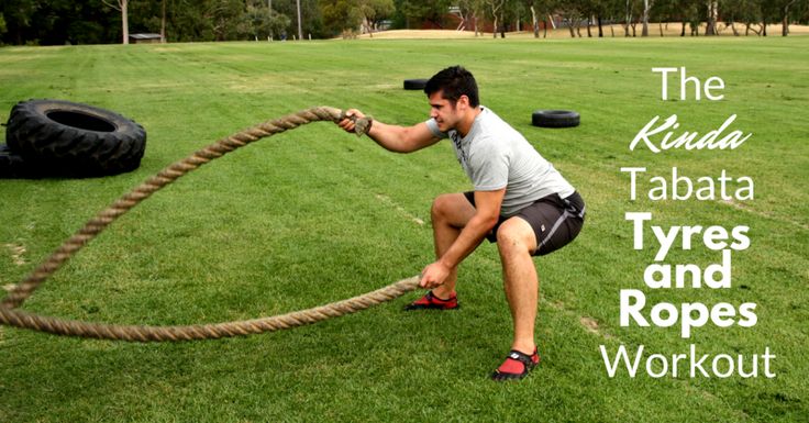 a man is pulling on a rope in the middle of a field with tires behind him