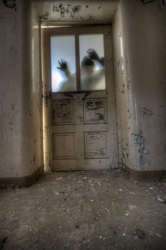 an open door with two hands coming out of it in the middle of a run down room