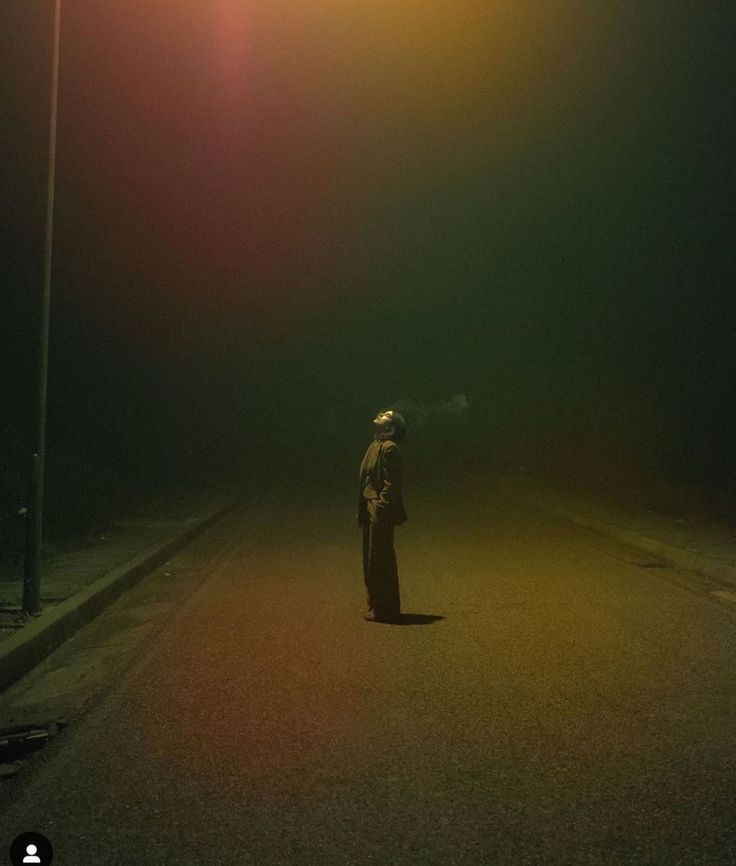 a person standing in the middle of an empty road at night with street lights on