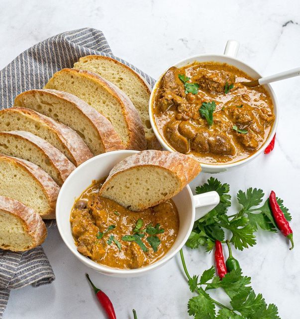 two bowls filled with soup next to slices of bread on a towel and red chili peppers