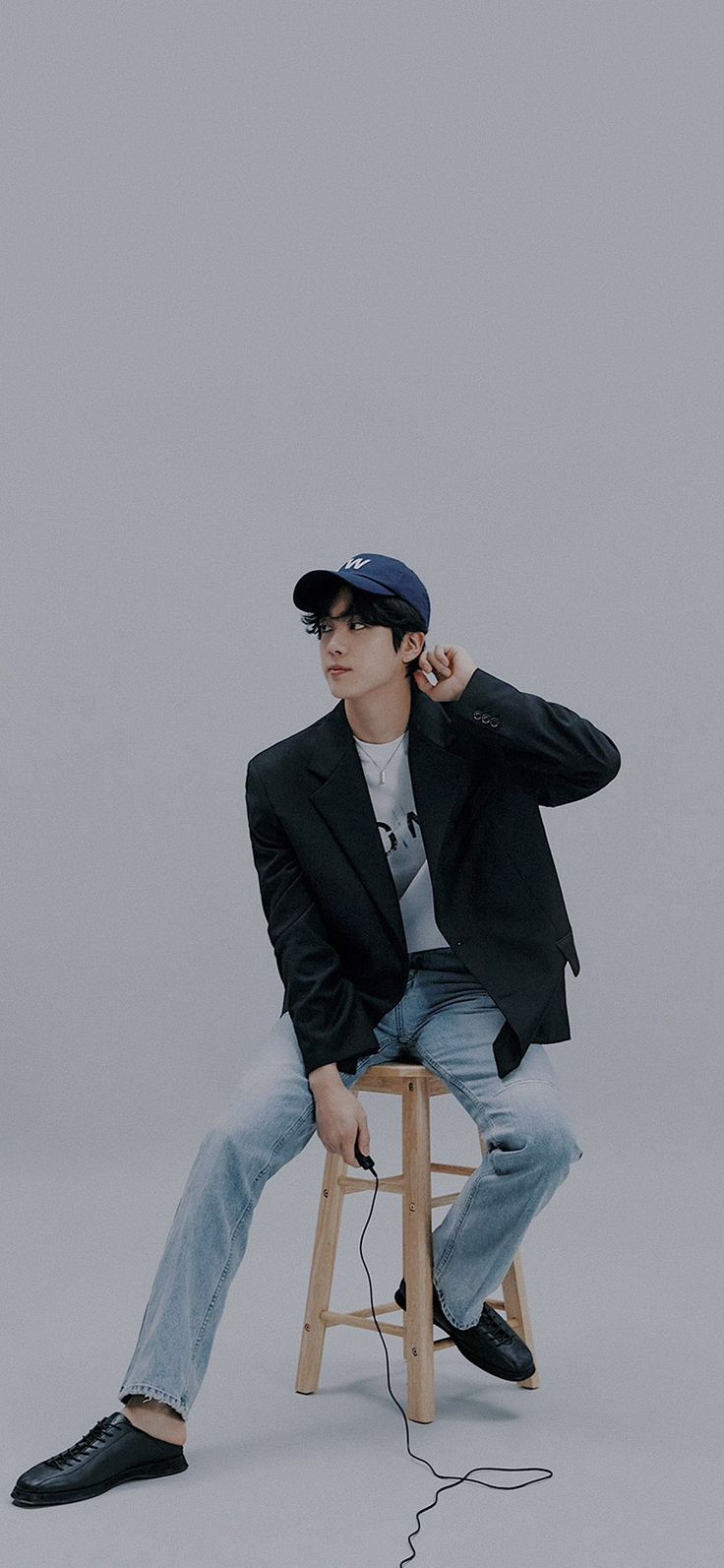 a young man sitting on top of a wooden stool wearing a baseball cap and jacket