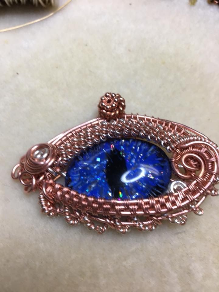 a wire wrapped brooch with a blue eye in the center on a white surface