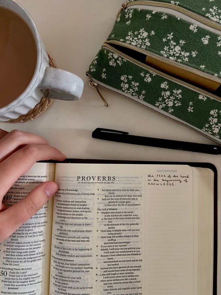 a person is holding an open book next to a cup of coffee