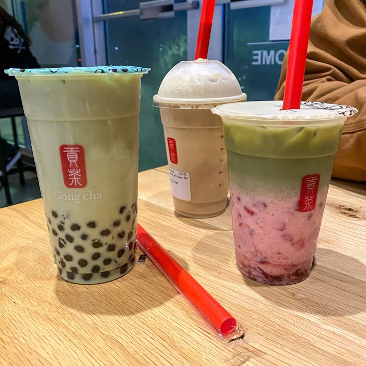 three drinks sitting on top of a wooden table next to each other with straws