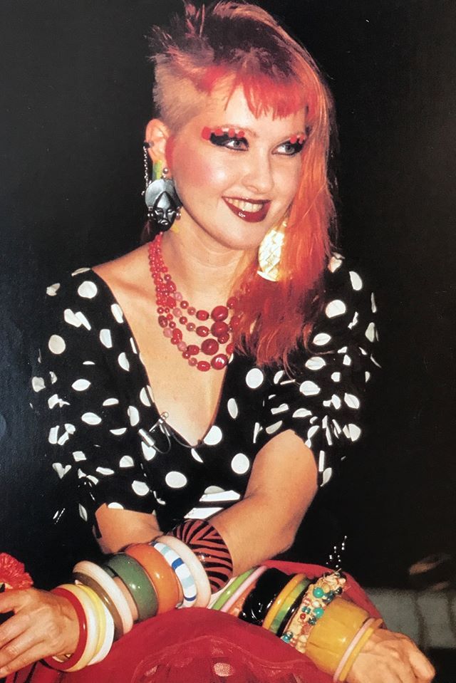 a woman with bright red hair and black polka dot shirt sitting in front of a table