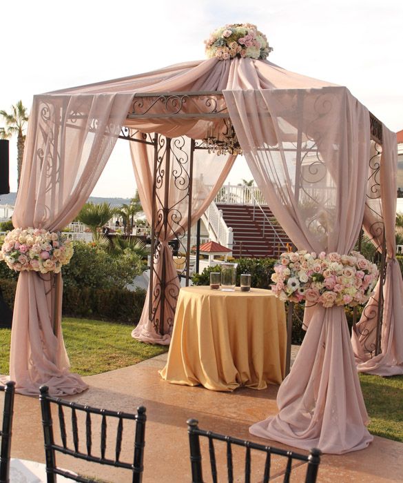 an outdoor wedding setup with pink drapes and white flowers on the table cloths