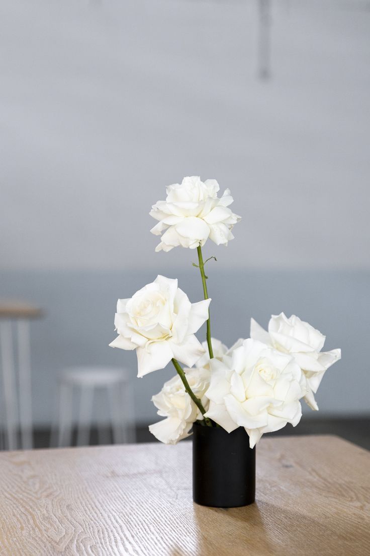 white flowers in a black vase on a wooden table