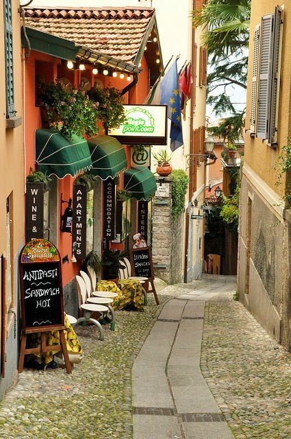 an alley way with tables and umbrellas on the side walk, next to buildings