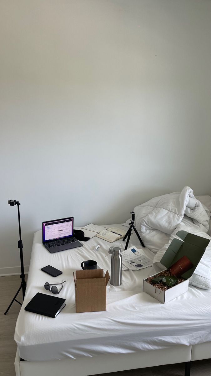 a bed with white sheets and various items on it, including an open laptop computer