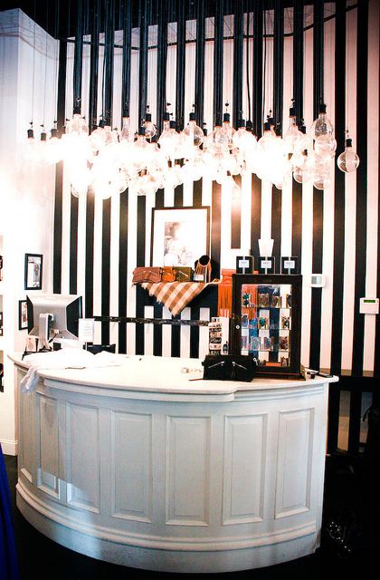 a black and white striped wall behind a reception desk with lights hanging from the ceiling