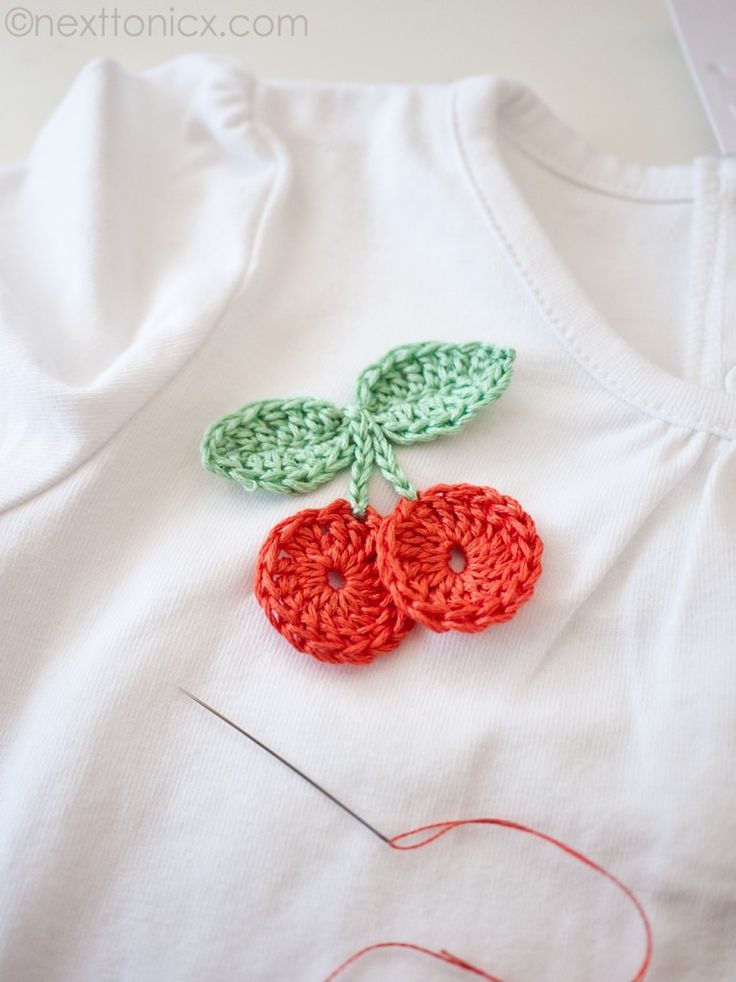 crocheted cherry applique on white shirt with red thread and green leaves