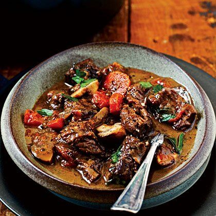 a bowl filled with meat and vegetables on top of a wooden table next to a spoon