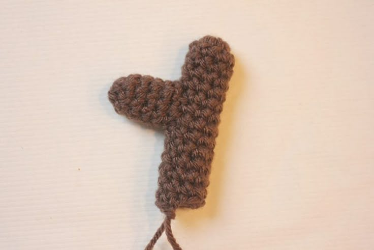 a crocheted brown object is hanging on a white wall with a tassel