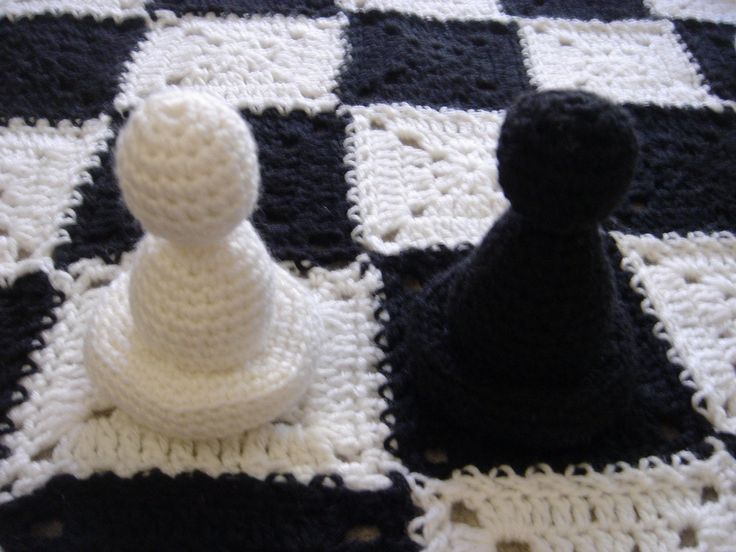 two crocheted chess pieces sitting on top of a black and white checkered blanket