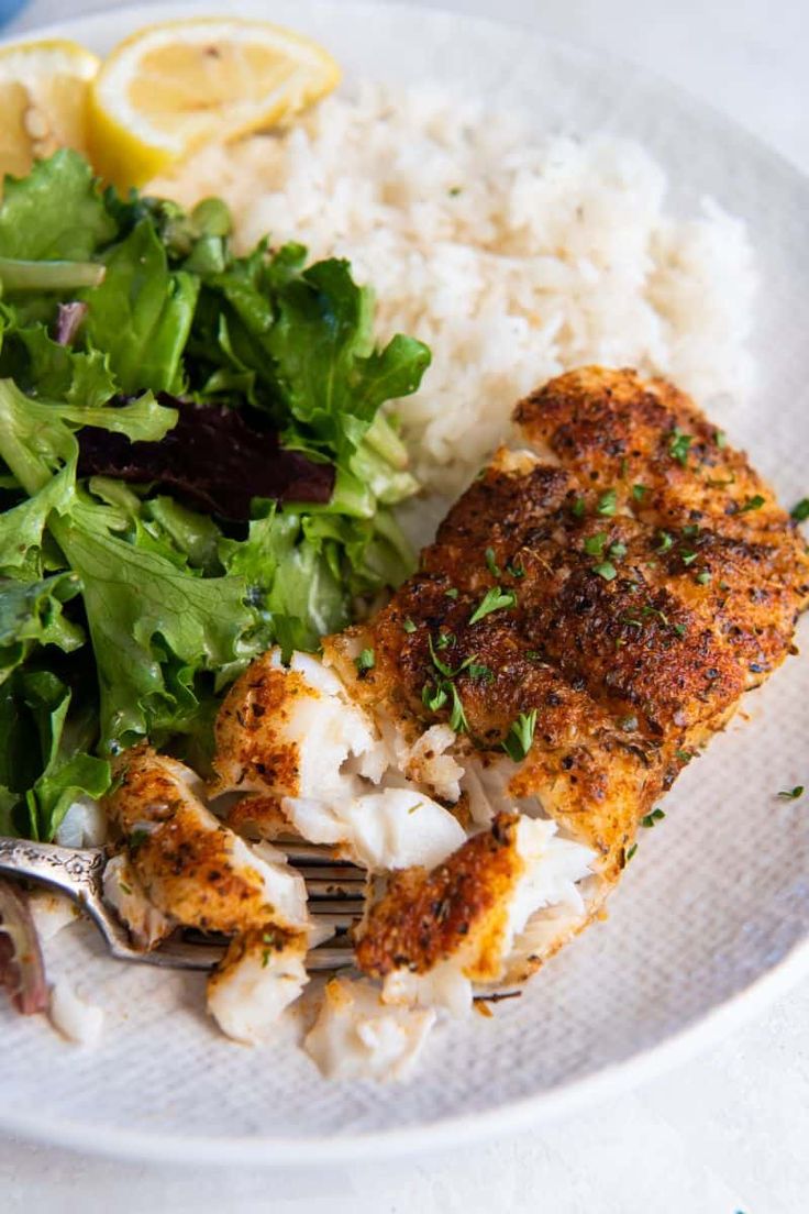 a white plate topped with chicken, rice and salad next to a lemon wedged slice