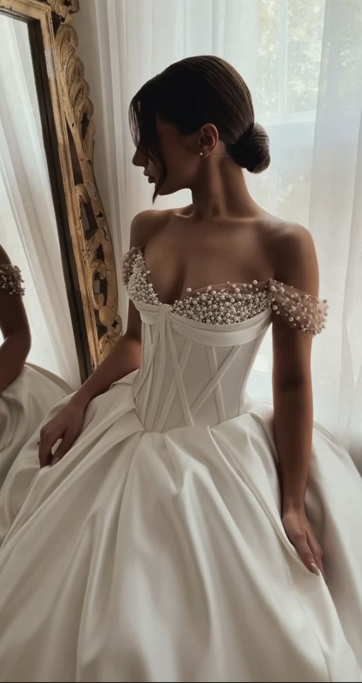 a woman in a white wedding dress looking at herself in the mirror with her hand on her hip