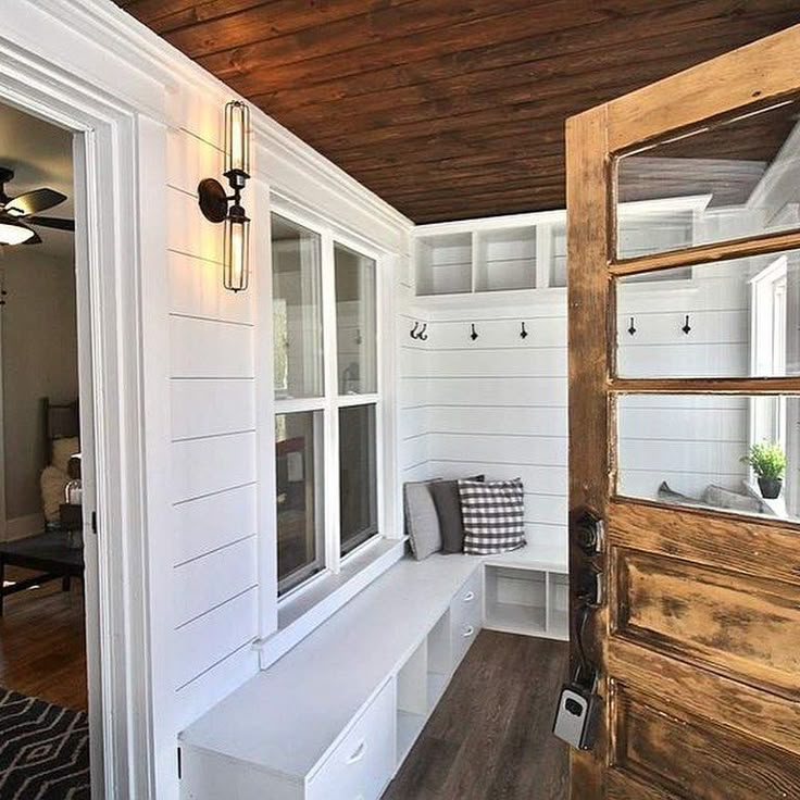 the inside of a home with white walls and wood floors, windows, and bench