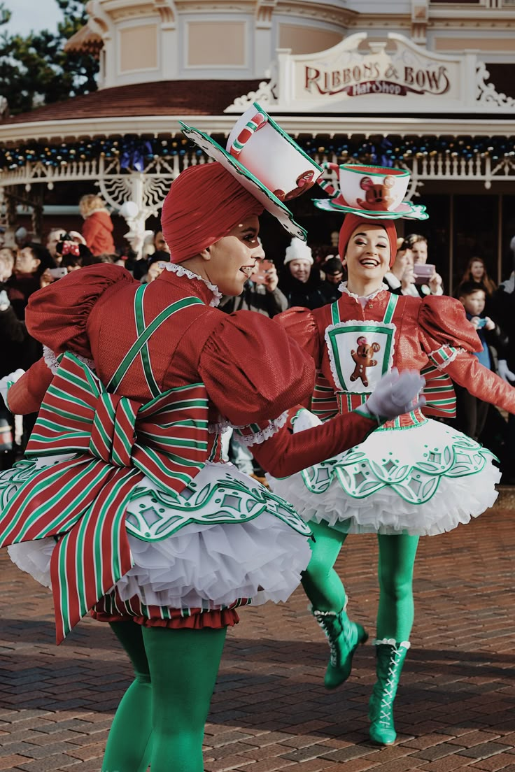 two people dressed in colorful costumes and green tights, one holding a cup while the other is dancing