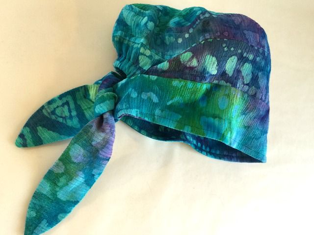 a green and blue tie - dyed hat laying on top of a white bed sheet