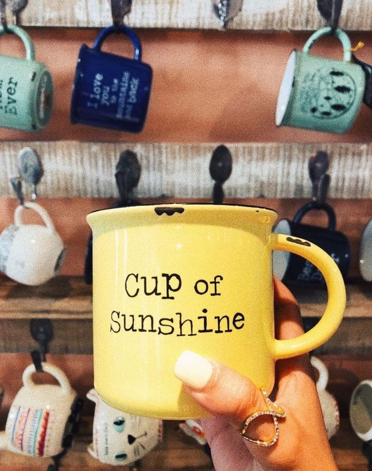 a person holding a yellow coffee mug with the words cup of sunshine on it