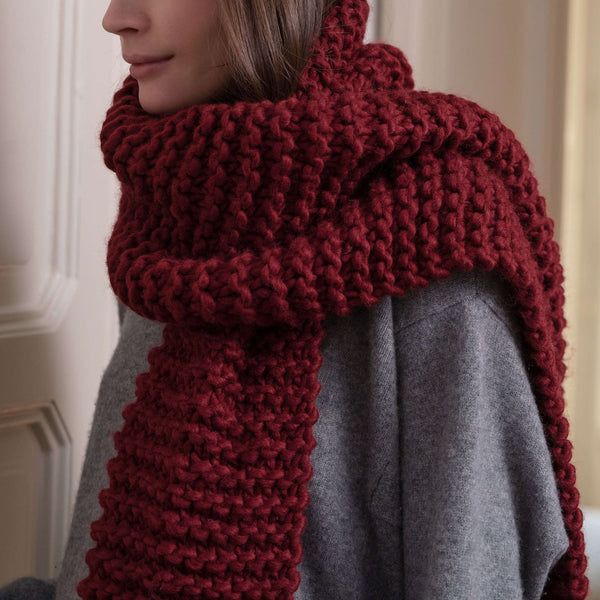 a woman wearing a red knitted scarf with a cowl around her neck, looking off into the distance