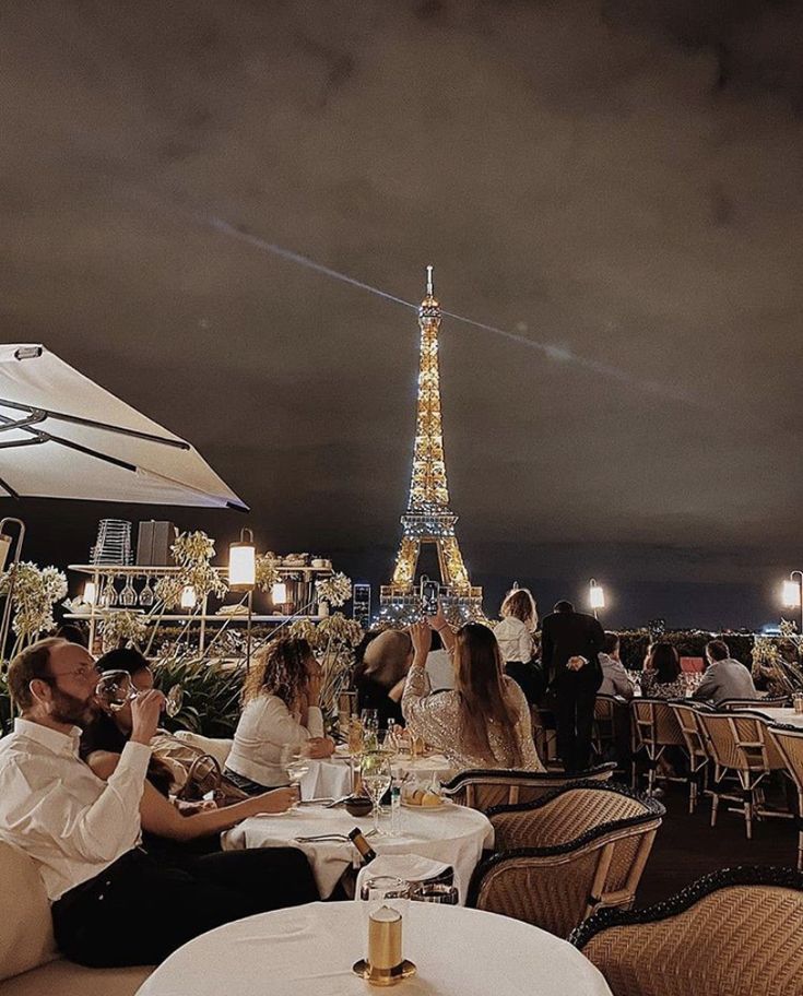 people are sitting at tables in front of the eiffel tower, eating and drinking