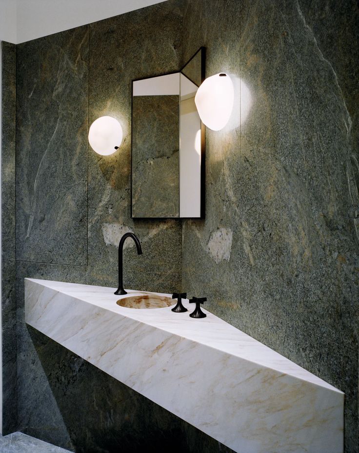 the green marble - clad powder room features a polished marble marble basin and black faucet