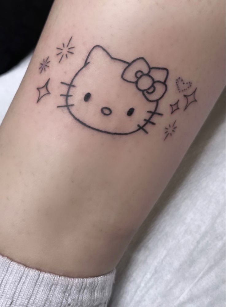 a small hello kitty tattoo on the arm with stars and sparkles around it's head