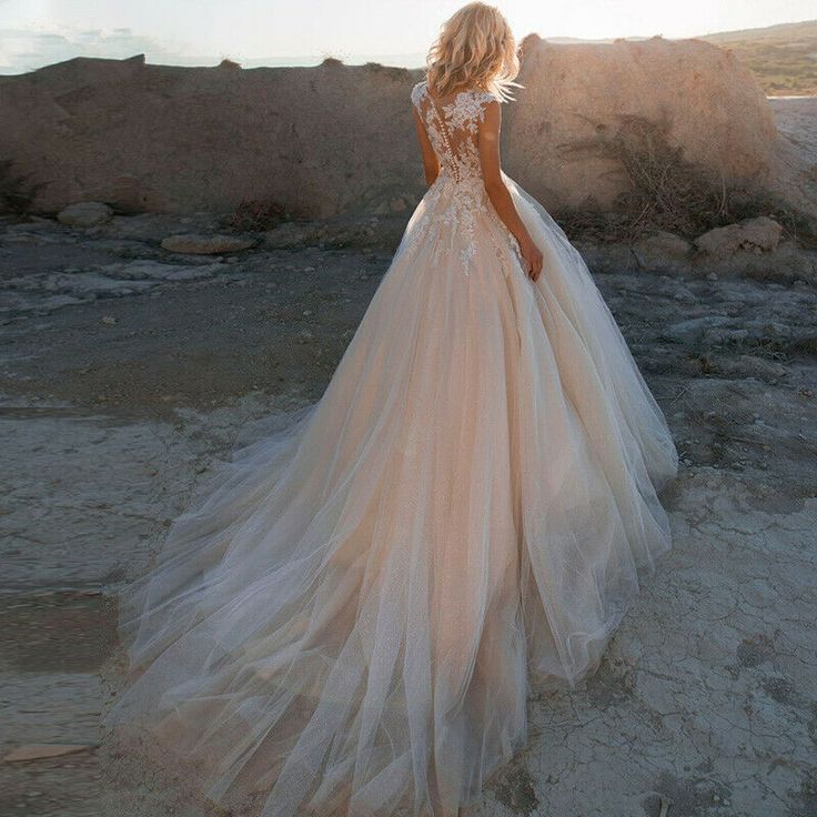 a woman in a wedding dress is standing on the beach with her back to the camera