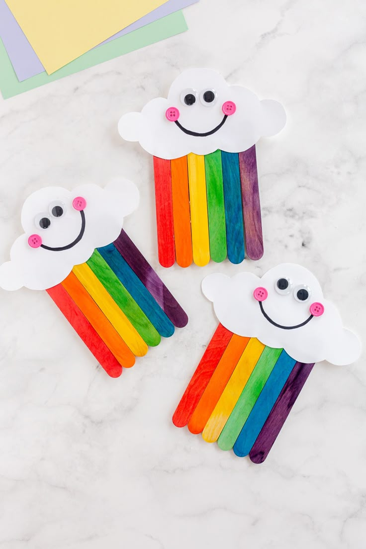 three pops sticks with rainbows and clouds painted on them sitting on a marble surface