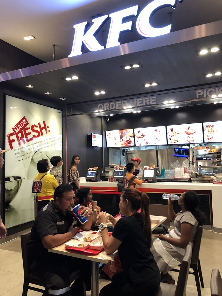 people sitting at tables in front of a fast food restaurant with the kfc sign above it