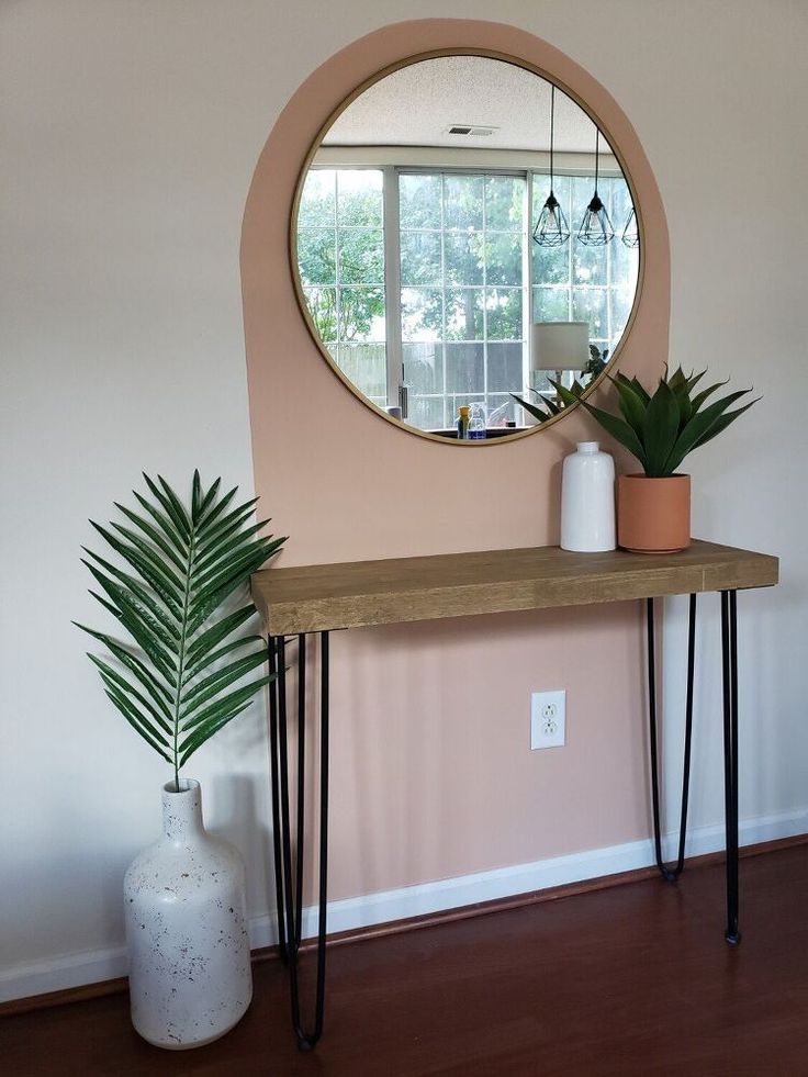 there is a mirror on the wall above a table with two plants and a vase