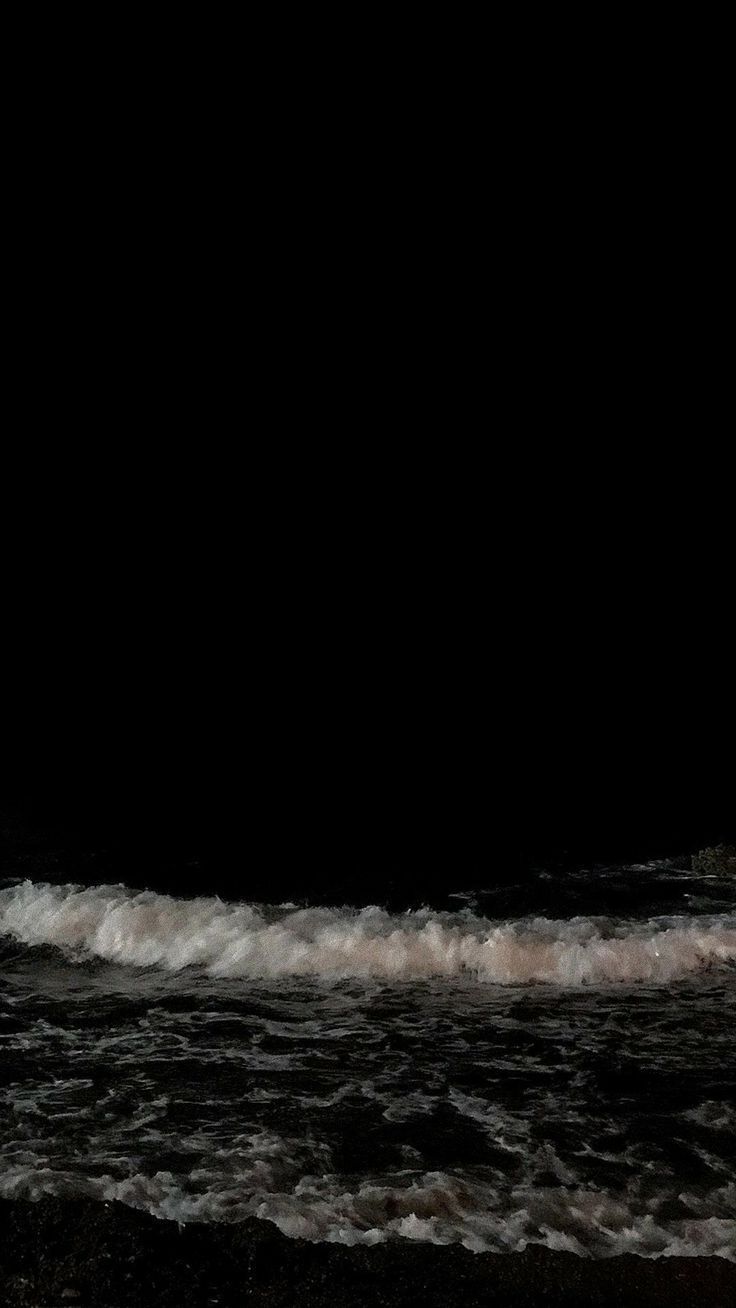 a man standing on top of a surfboard next to the ocean in the dark