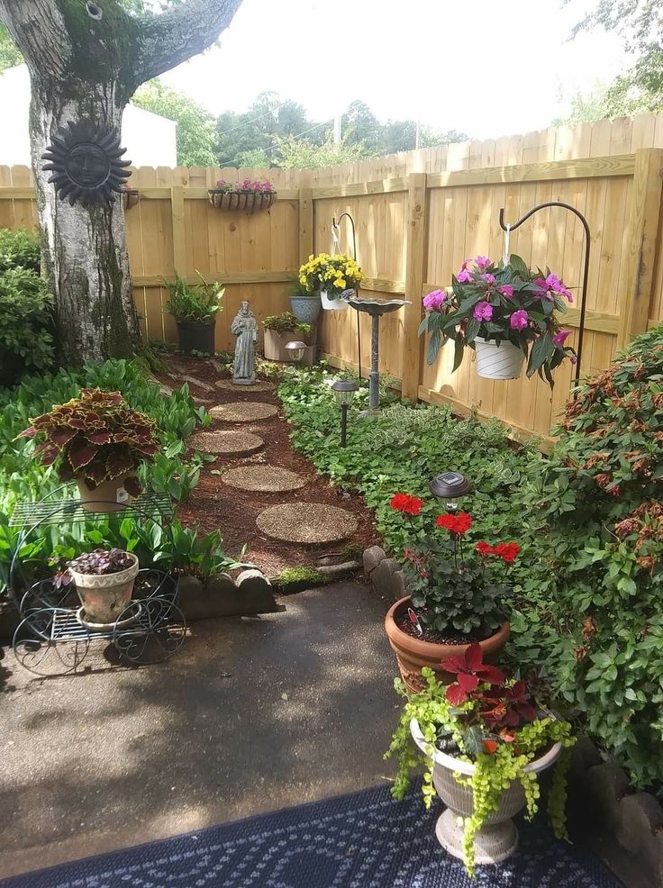 a garden with lots of flowers and plants on the ground near a fenced in area