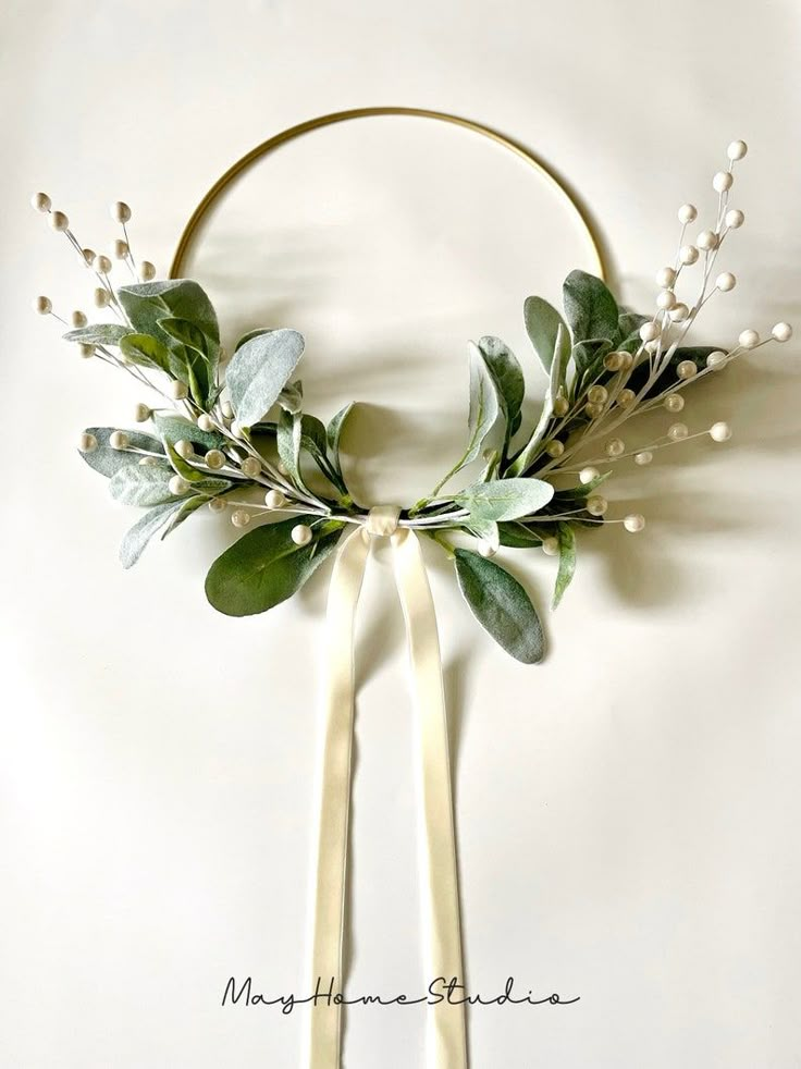 a wreath with white flowers and greenery is hanging on the wall next to a hoop