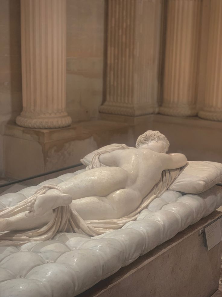 a white statue laying on top of a bed in a room with columns and pillars