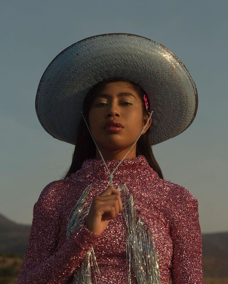 a woman wearing a large hat with tassels around her neck and holding a string