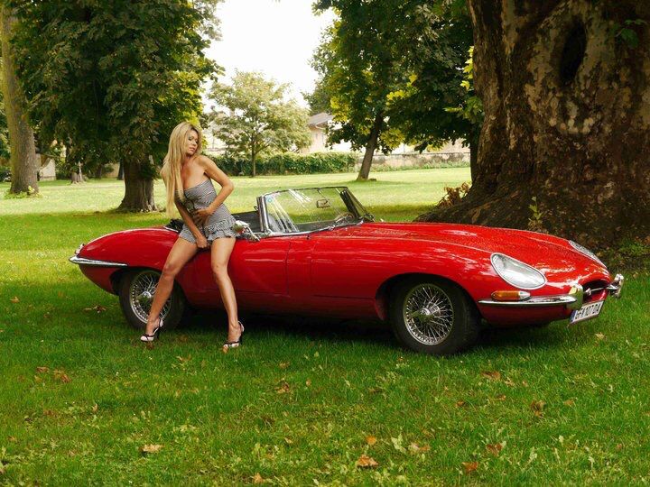 a woman leaning on the hood of a red sports car in front of a tree