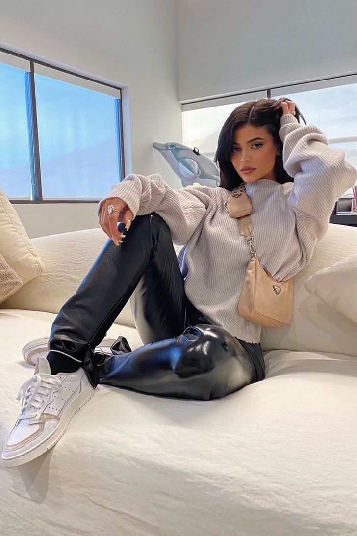 a woman sitting on top of a bed wearing black leggings and holding a purse