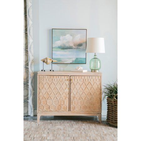 a sideboard with a painting on the wall behind it and a lamp next to it