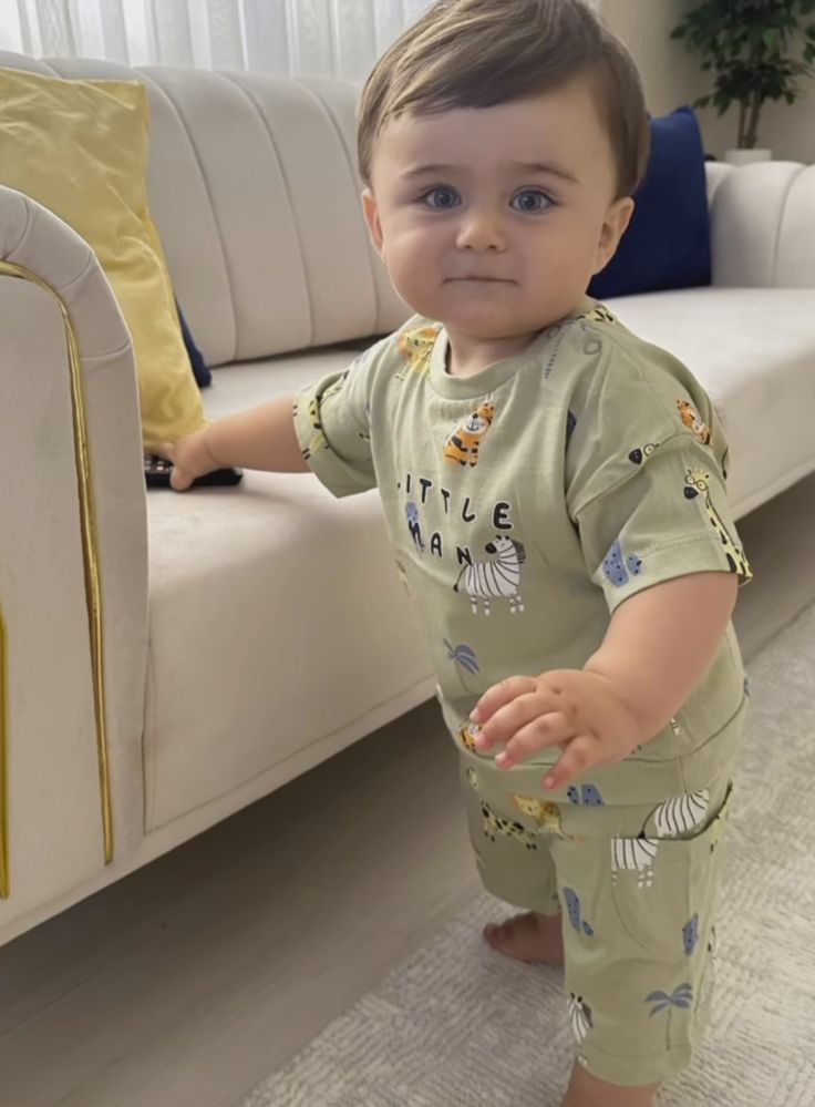 a little boy standing in front of a couch with his foot on the floor and looking at the camera