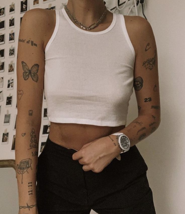 a woman with tattoos on her arms and chest standing in front of a white wall